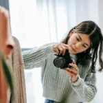 Fotografer perempuan mengambil foto produk baju yang tergantung di rak di ruang studio berpendar terang